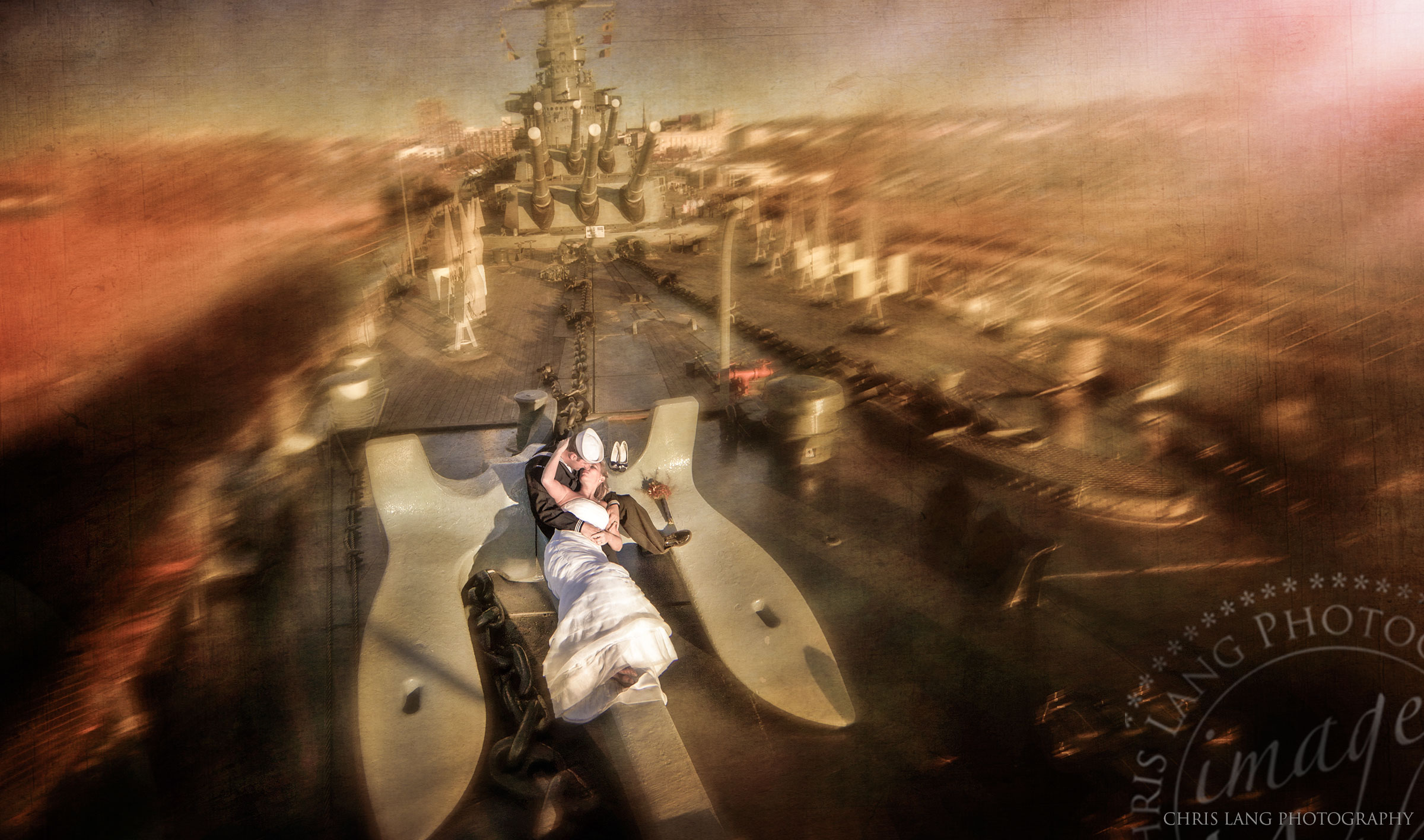 A low level aerial wedding picture of a wedding coulple kissing on a the deck of a battleship while sitting on an anchor.  Wilmington Wedding Photographers