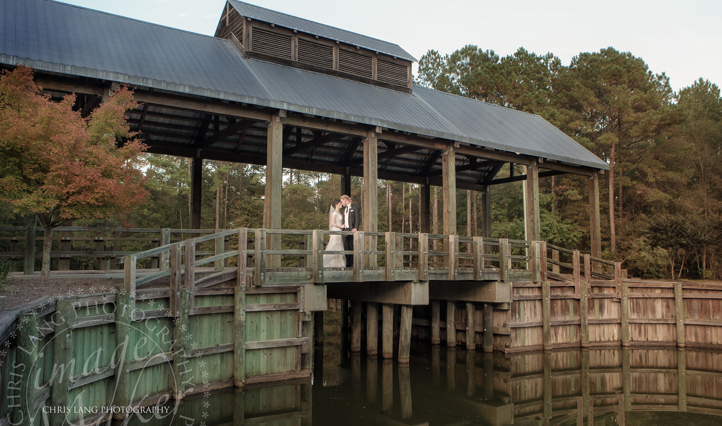 A classic wedding picture of a bride and groom standing on a covered bridge over the water.  River Landing Wedding Photographers