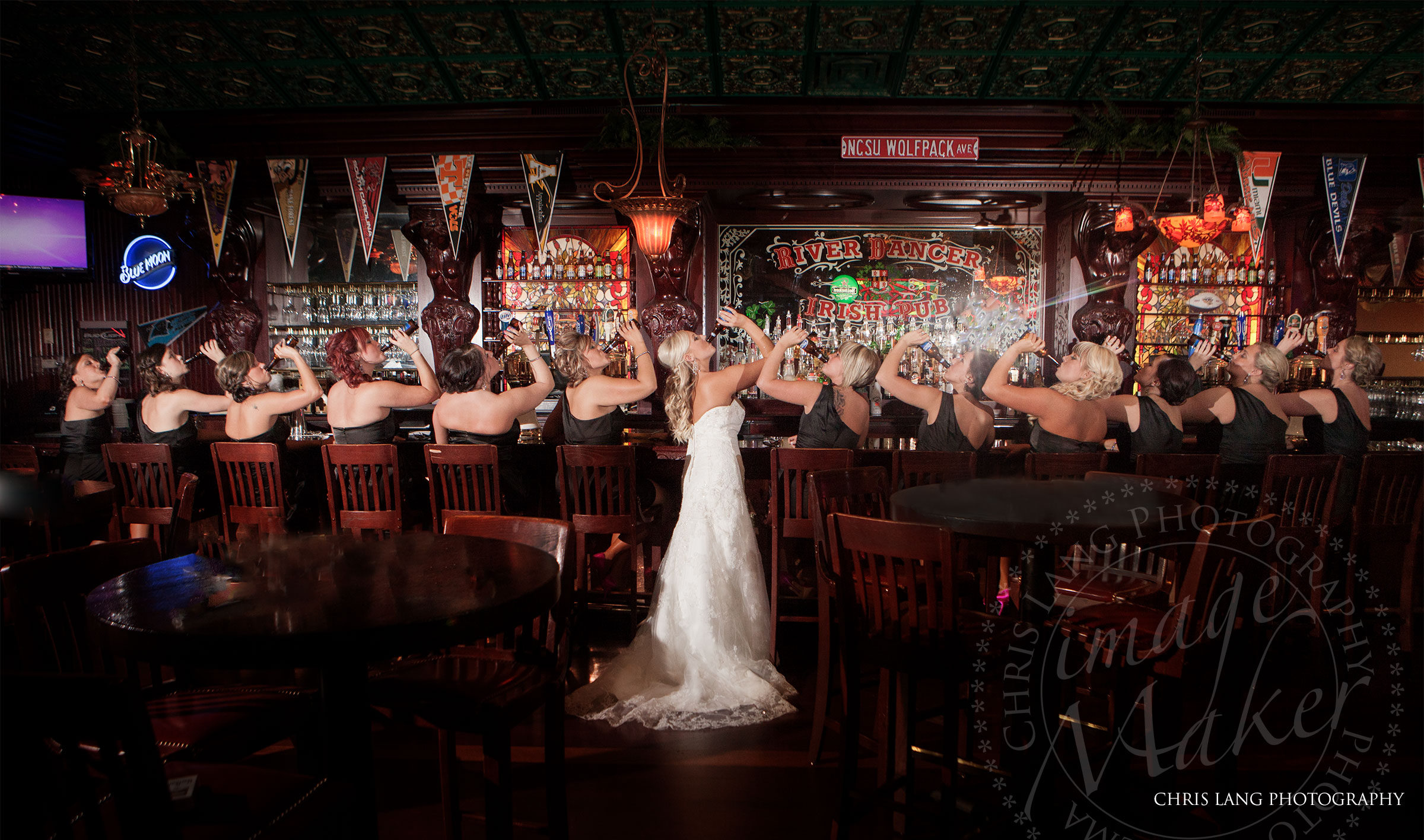 a fun wedding picture of a bride and bridesmaids lifting ber bottles in the air for a toast while sitting at the bar.  Wilmington NC Photographer