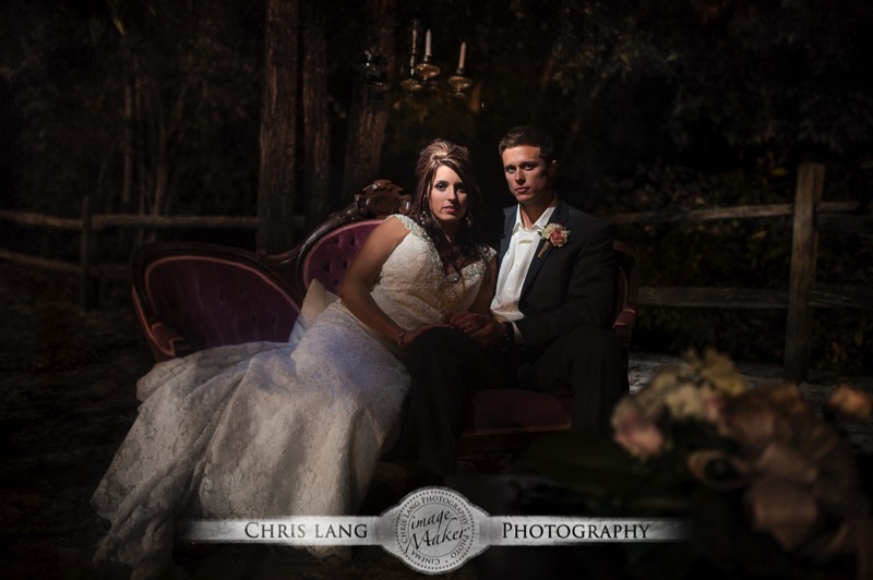 A romantic wedding picture of newlyweds on a counch outside at night lit by a chandelier hanging from a tree.  Wedding ideas.  