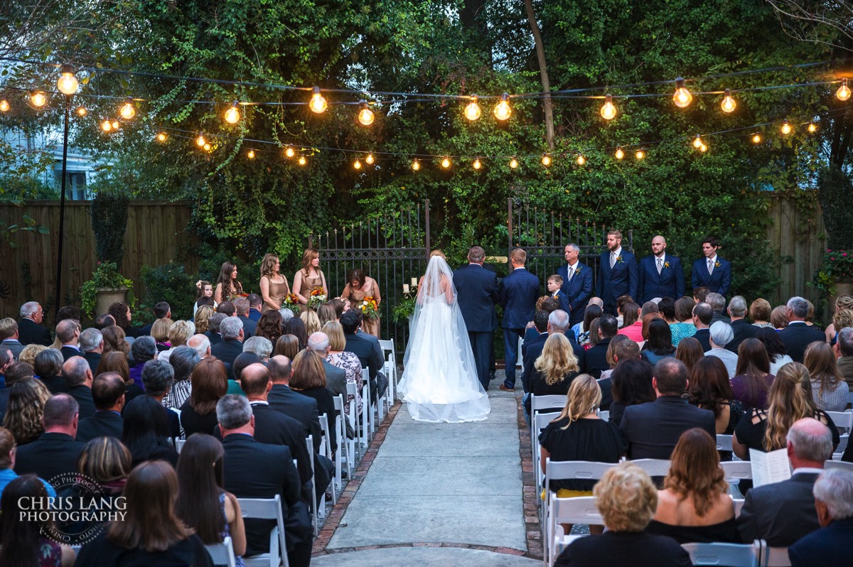 A evening wedding ceremony in the courtyard at Brooklyn Arts Center - Edison lighting - outdoor wedding - father walking bright down the isle - weddings - wedding venue -  wedding photo - bride - groom - ideas - wilmington nc - chris lang photography 
