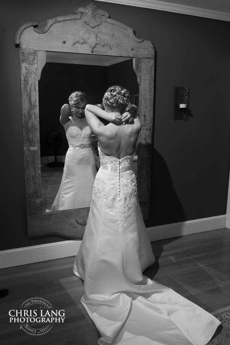 bride putting on jewlelry in mirror  - pre wedding photos - wedding photo ideas - getting ready wedding pictures - bride - groom - wedding dress - wilmington nc wedding photography  