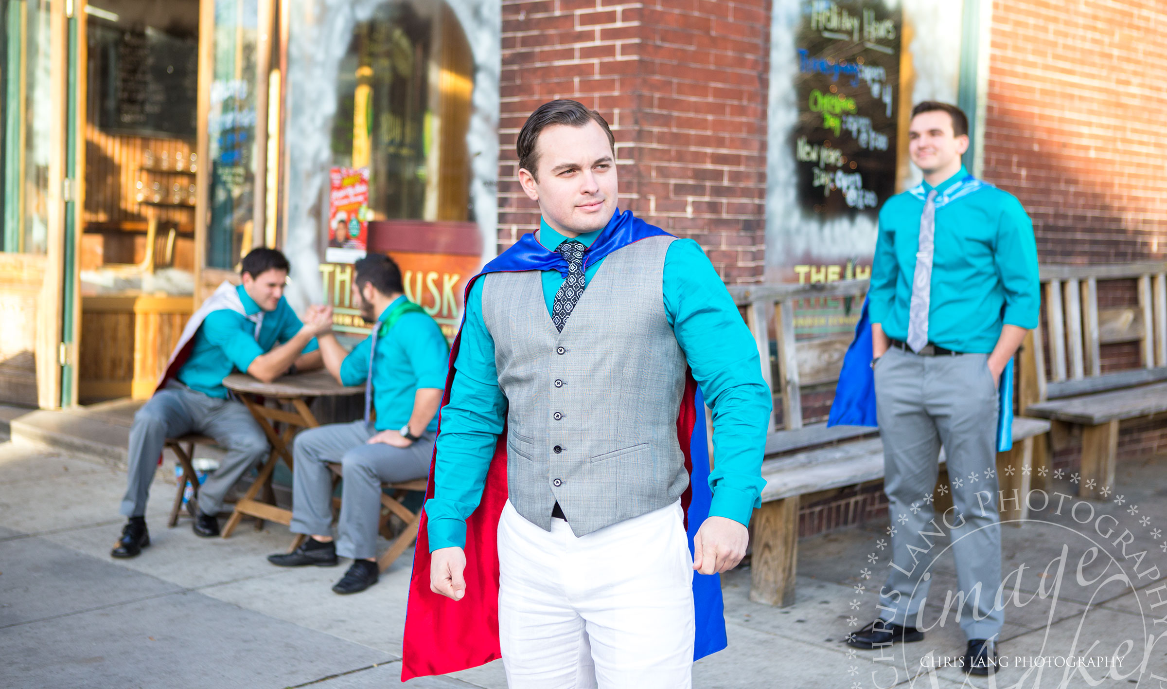 A fun wedding picture of a groom wearing a super hero cape in front of The Balcony on Dock. Wilmington NC wedding photographers