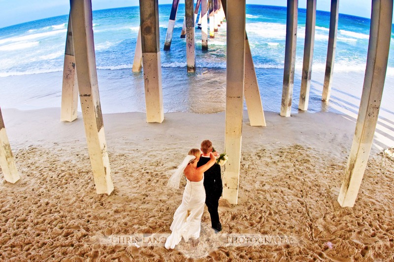 Wedding picture of a couple under a pier at Wrightsville Beach looking out to the Atlantic Ocean. Beach wedding photography