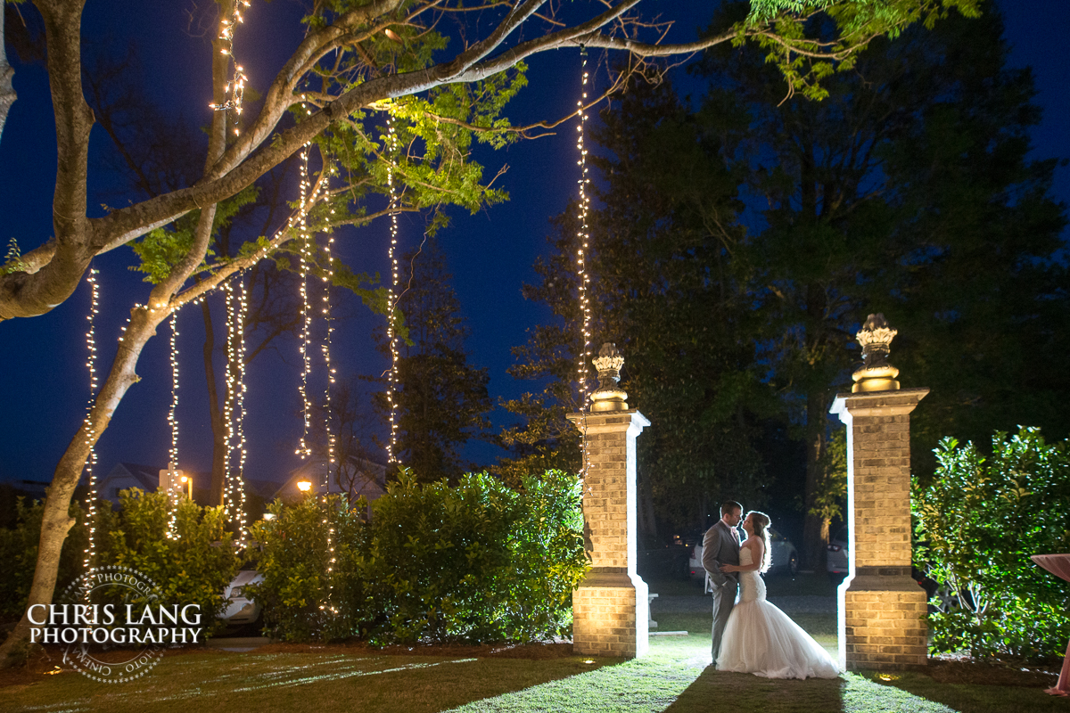 image of bride and groom underneath the giant oak tree with hanging lights. Wrightsvile Manor Wedding Venue - Wilmington NC Wedding Photography 
